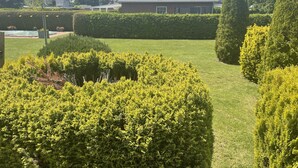 Ein gepflegter Garten mit ordentlich geschnittenen Hecken und einem Rasen, der zu einem Haus mit einem Ziegeldach und Dachgauben führt.