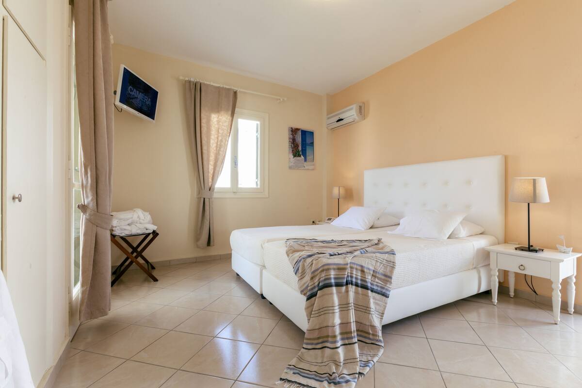 Une chambre à coucher avec un lit, une table de chevet, une télévision et une fenêtre avec des rideaux.