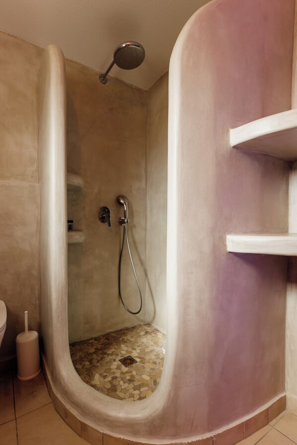 Une douche au design incurvé, une douchette à main et un sol carrelé.