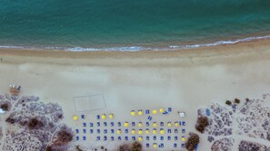 Di pantai, pasir putih, kursi berjemur, dan payung pantai