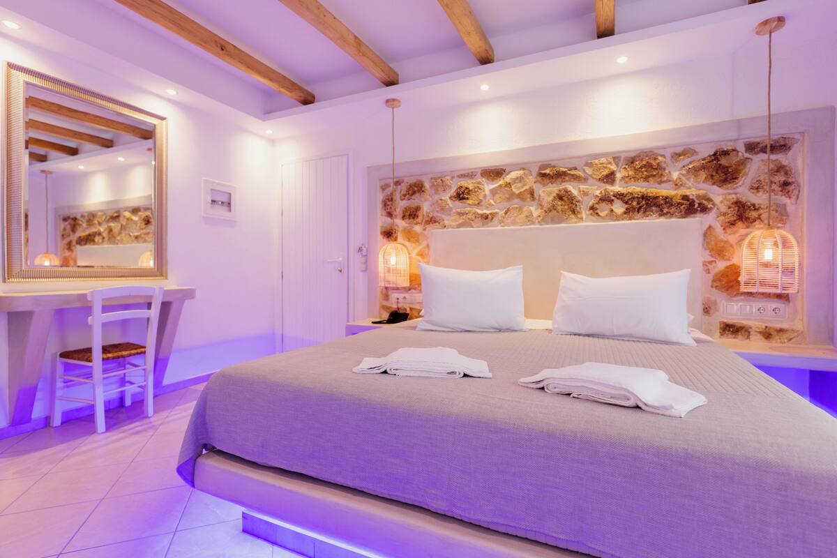 Une chambre avec un mur en pierre, un lit avec du linge de lit blanc, un bureau avec une chaise et un miroir.