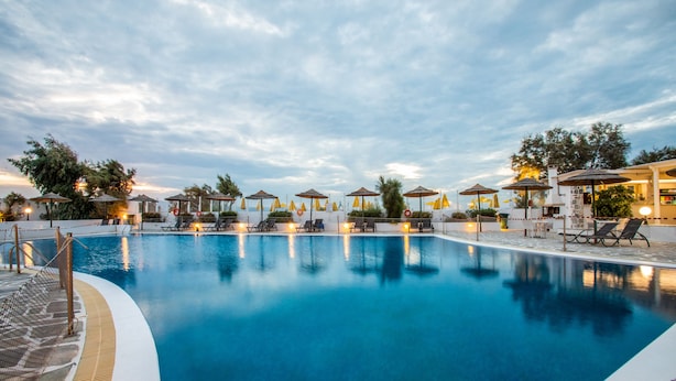 A swimming pool with lounge chairs and umbrellas, surrounded by a fence and trees. - Mikri Vigla Hotel Beach Resort (Naxos)