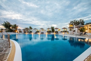 Une piscine entourée d’une clôture et d’arbres, avec des chaises longues et des parasols.