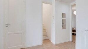Un pasillo con una puerta blanca, una escalera y un estante en la pared.