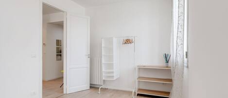 Una stanza con un armadio bianco, una scaffalatura bianca e una porta che dà su un'altra stanza.