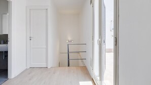 Un pasillo con una puerta blanca, una puerta de vidrio y un perchero metálico.
