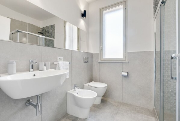 Un baño moderno con un lavamanos grande, un bidé, un inodoro y una ducha con mampara de vidrio.