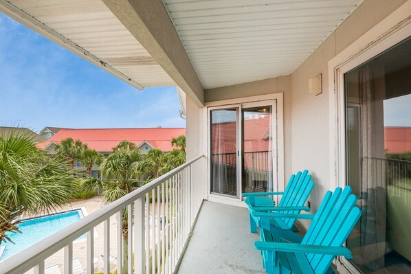 A balcony with a pool view, blue chairs, and a red-roofed building in the background. - 🐟Walk to Beach~Pool + Corner Balcony~PRIME Location~Rollin Tide B9 (Santa Rosa Beach)