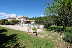 Una casa con piscina, rodeada por un patio cercado y árboles.