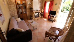Una sala de estar acogedora con pared de piedra, chimenea, televisión y sillón de mimbre.