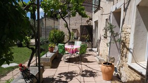 Un patio al aire libre con una mesa y sillas, rodeado de plantas en macetas y un muro de piedra.