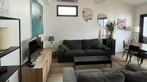 A modern living room with a sofa, coffee table, and TV. There is a ceiling fan, artwork, and a window. - Charming villa in Cap-Ferret (Lège-Cap-Ferret)
