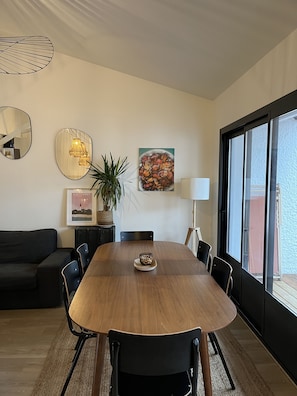 Uma sala de jantar moderna com uma mesa de madeira, cadeiras pretas, uma planta em vaso e obras de arte nas paredes.