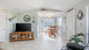 A living room with a TV, wooden cabinet, and a dining area with chairs.