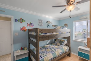 Un lit superposé avec une couvre-lit matelassé, un ventilateur de plafond et une fenêtre avec des stores.
