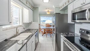 A modern kitchen with white cabinets, a granite countertop, stainless steel appliances, and a view to the outside.