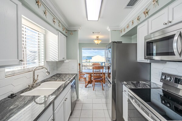 A modern kitchen with white cabinets, a granite countertop, stainless steel appliances, and a view to the outside.