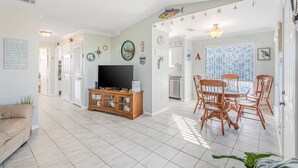 A spacious living room with a television, wooden cabinet, and a dining area with wooden chairs.