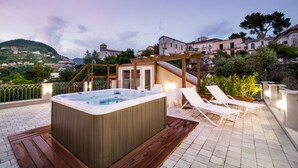 A rooftop terrace with a hot tub, lounge chairs, and a view of a hillside town.
