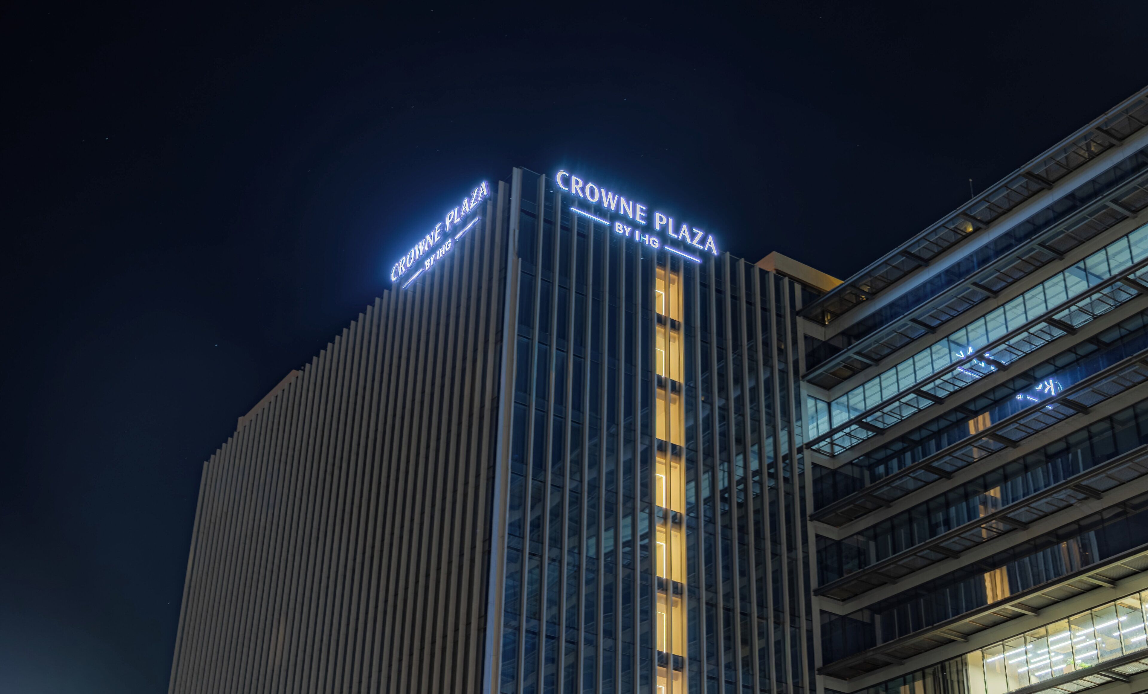 A modern building with vertical lines and illuminated signage reading "CROWNE PLAZA".