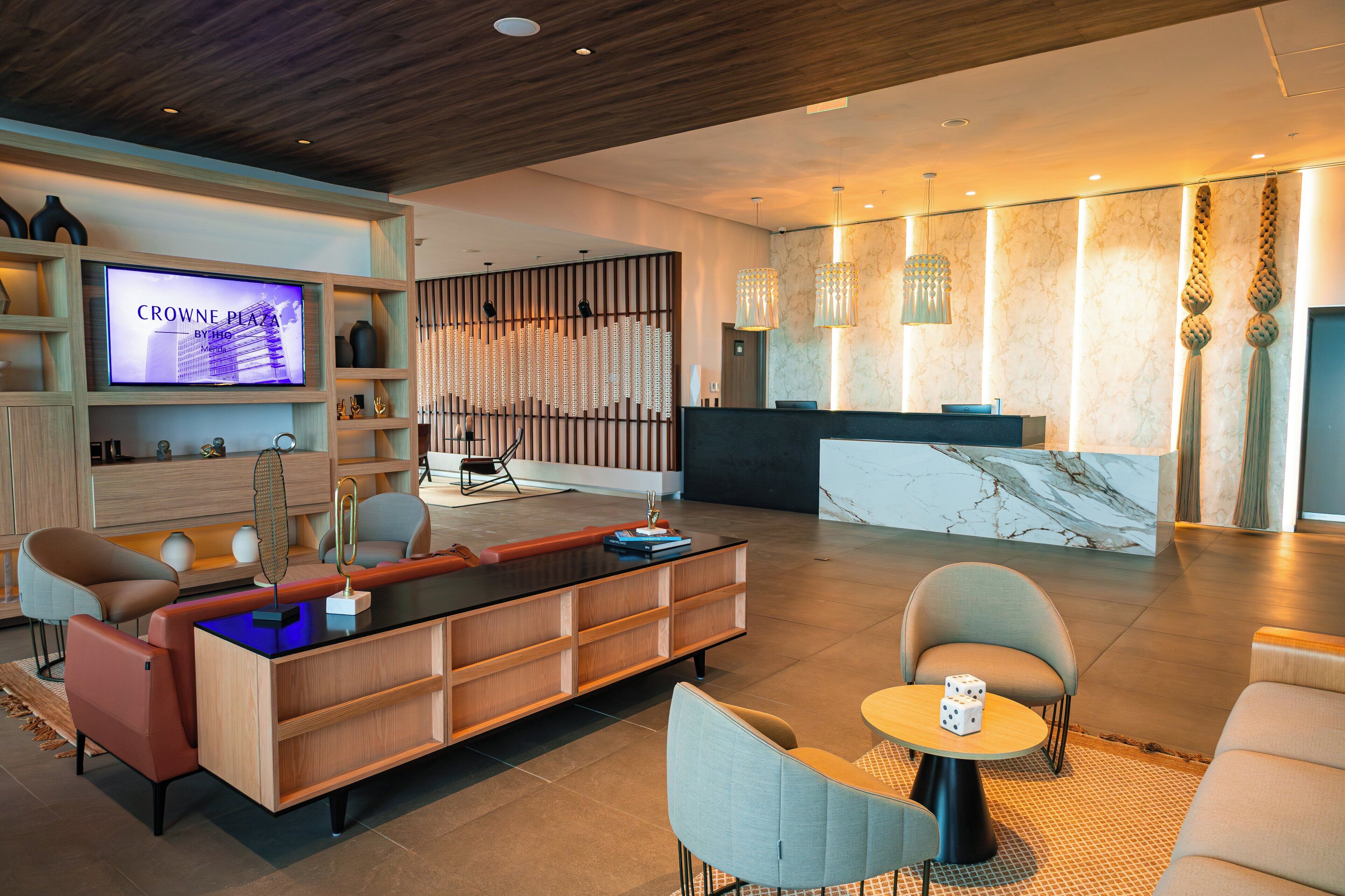 A modern lobby with a reception desk, seating area, and a television displaying 'CROWNE PLAZA'.