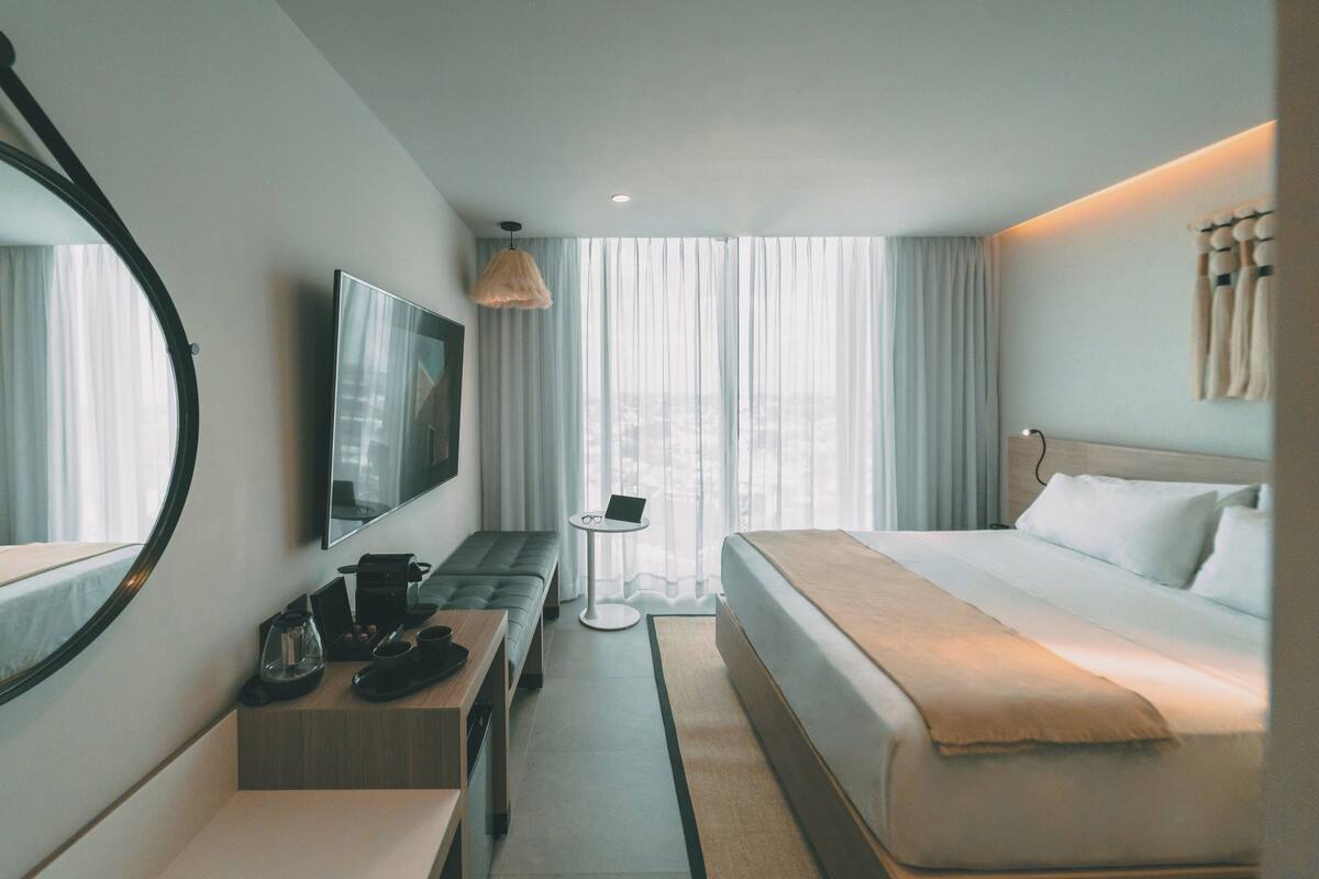 A hotel room with a bed, a desk with a laptop, a coffee maker, and a TV on the wall.