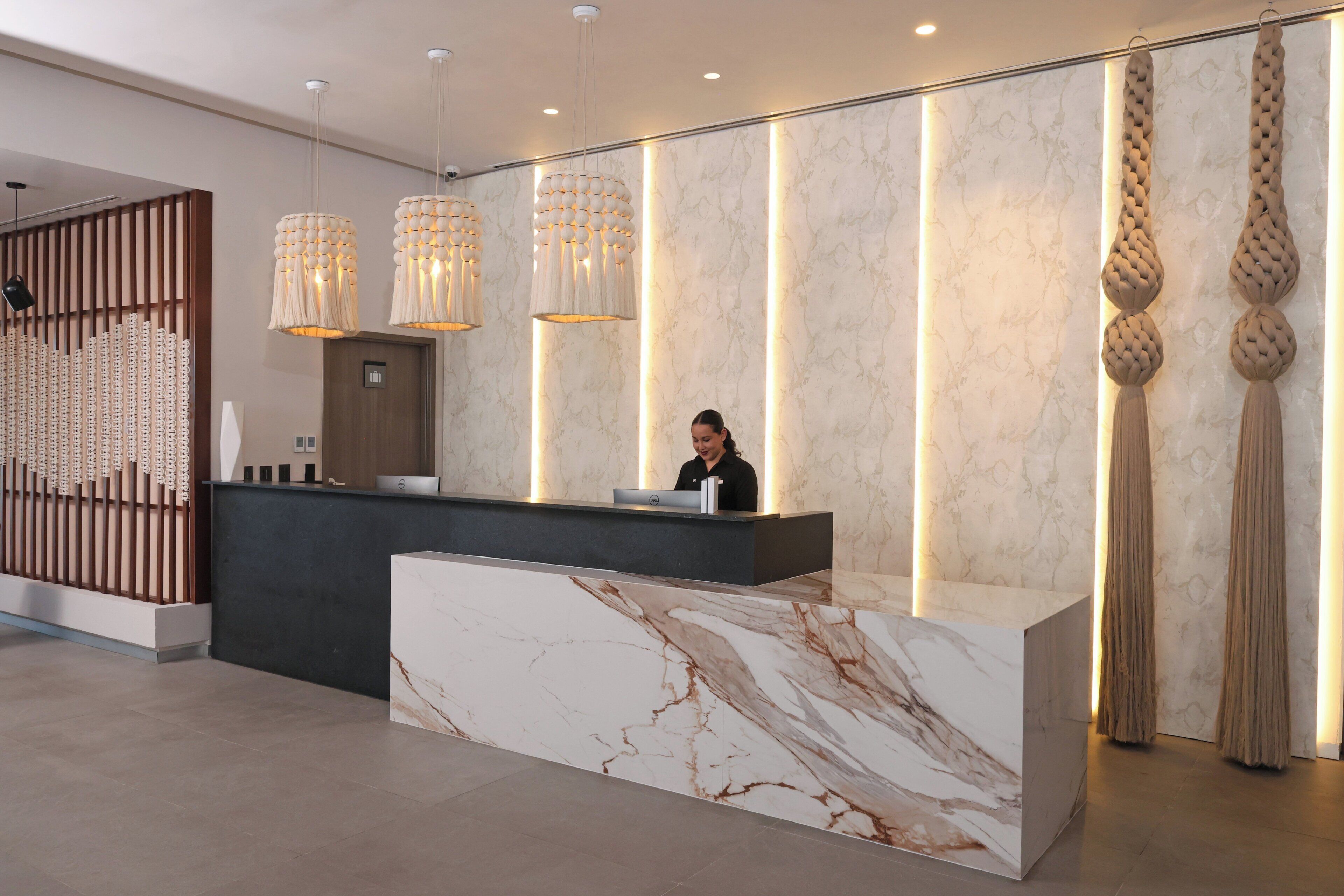 Una moderna recepción con encimera de mármol, una recepcionista e iluminación decorativa.