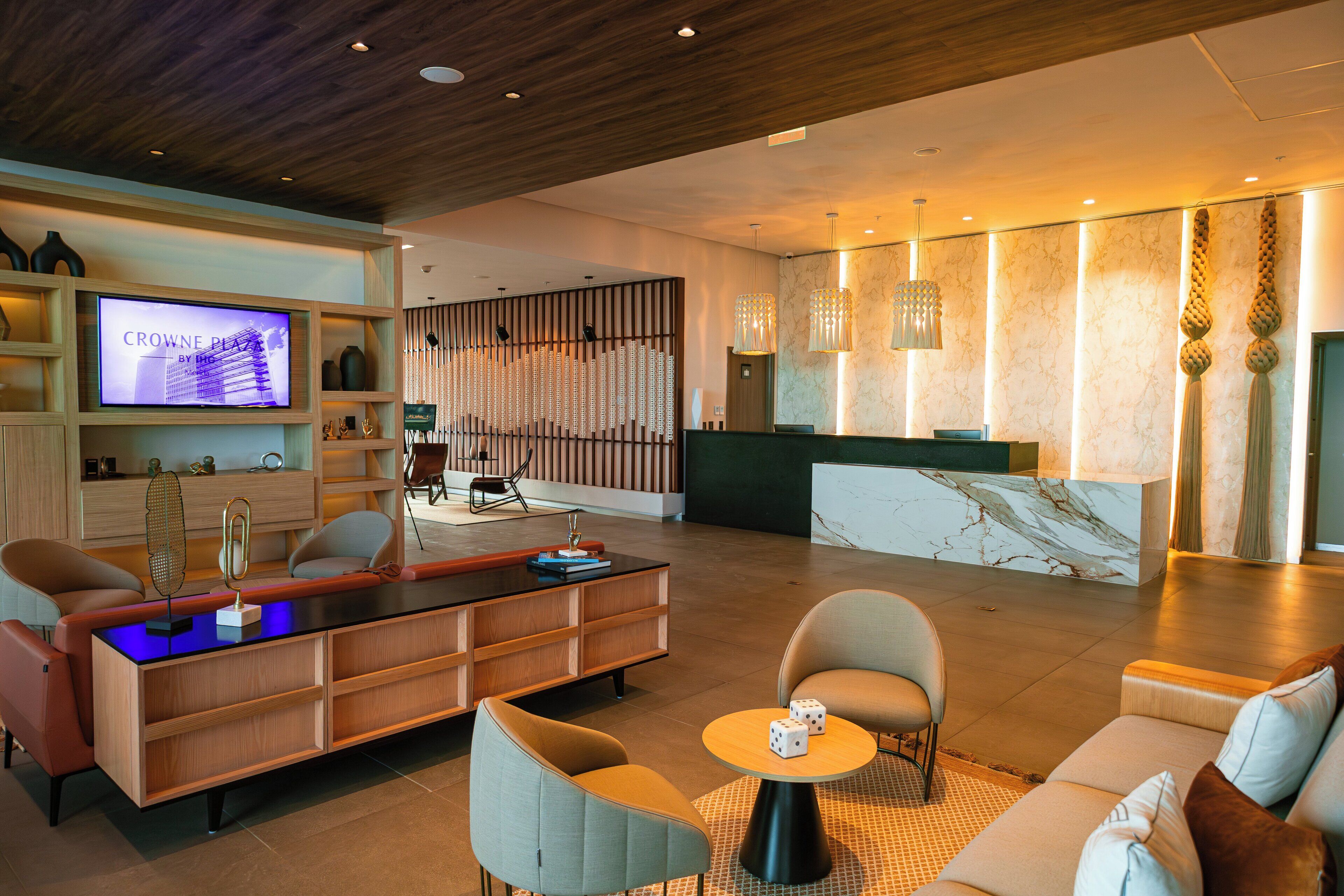 A modern lobby with a reception desk, seating area, and a television displaying 'Crowne Plaza by IHG'.