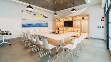 A modern conference room with a long table, white chairs, a large abstract painting, and a television on a wooden shelf.