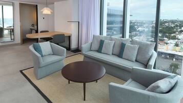 Una habitación de hotel moderna con un sofá, dos sillones, una mesa de centro y un comedor.