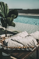 Una silla de mimbre con toallas blancas, una planta en maceta y una piscina al fondo.
