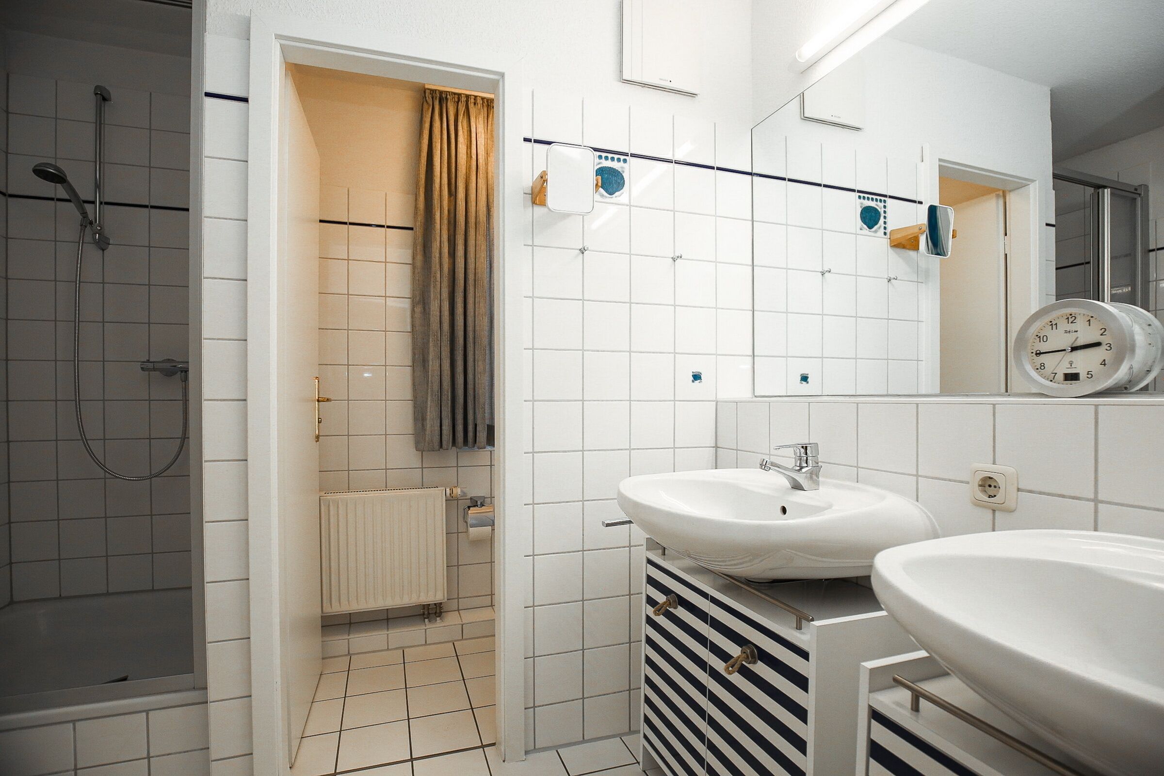 A modern bathroom with a shower, two sinks, a towel rack, and a clock on the wall.