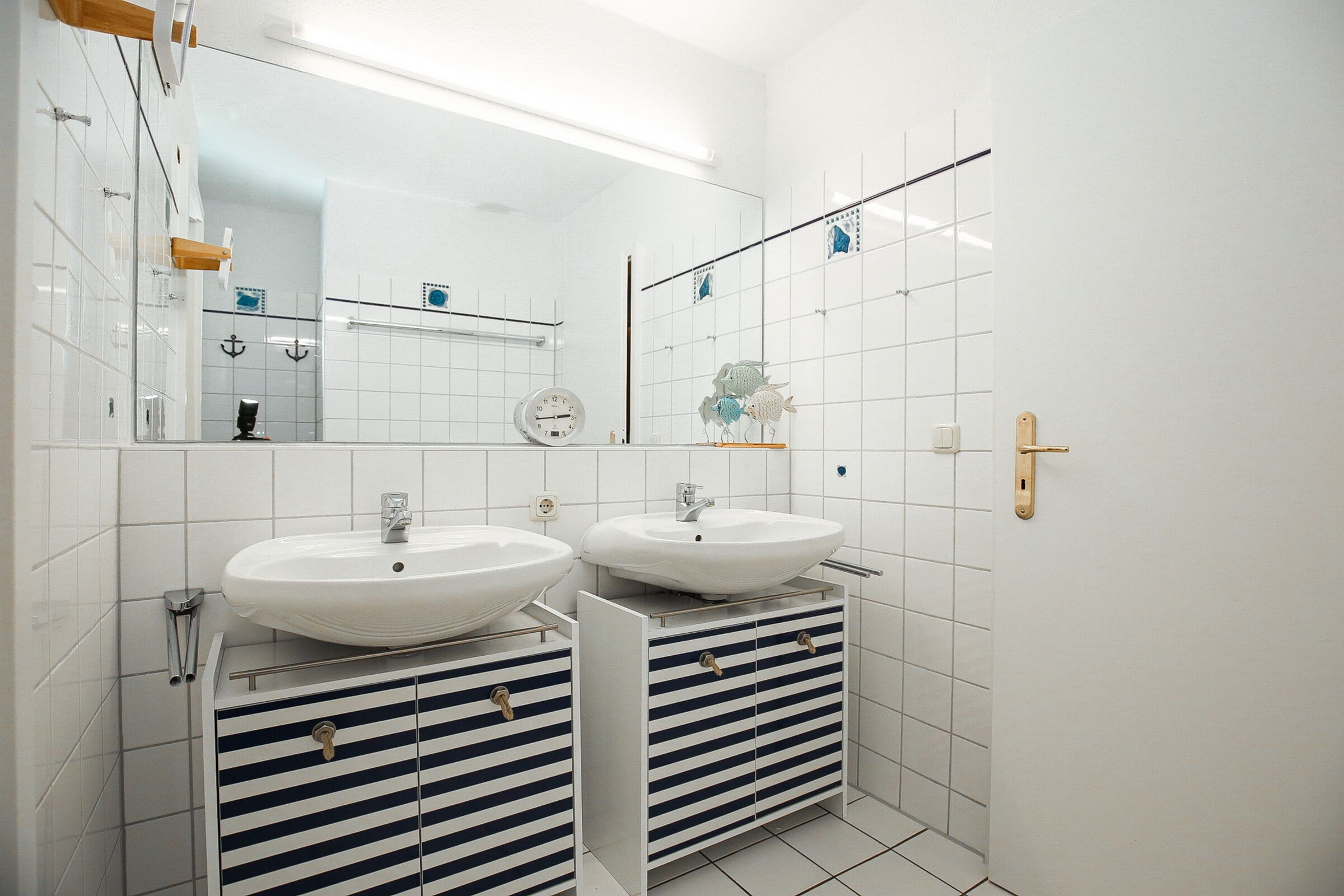 Une salle de bain moderne avec deux lavabos, un miroir et une horloge au mur.