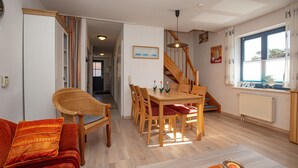 Un salón amplio con una mesa de comedor de madera, sillas con cojines rojos, un sofá de mimbre y una escalera que sube a otro nivel.