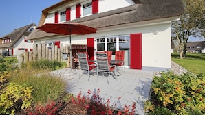 Une maison avec un patio, un espace salon extérieur et un parasol rouge.