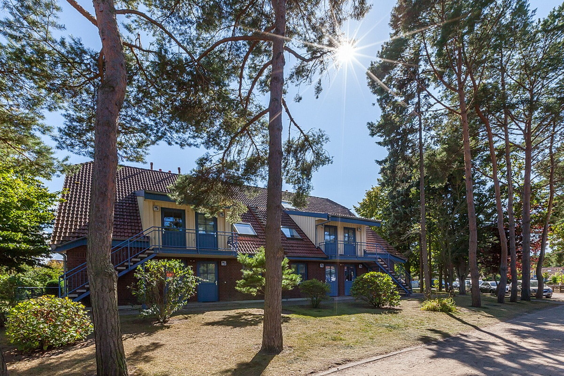 Ein zweistöckiges Gebäude mit rotem Ziegeldach, umgeben von hohen Bäumen und blauem Himmel.