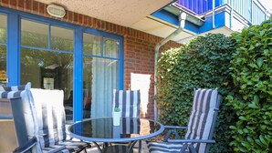 A patio with a round glass table and striped chairs, a brick wall, and a blue door. - Papillon Wohnung 07-2 (Ostseebad Boltenhagen)
