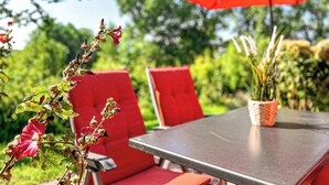 Ein Tisch mit einem roten Sonnenschirm, roten Stühlen und einem Blumentopf mit Blumen.