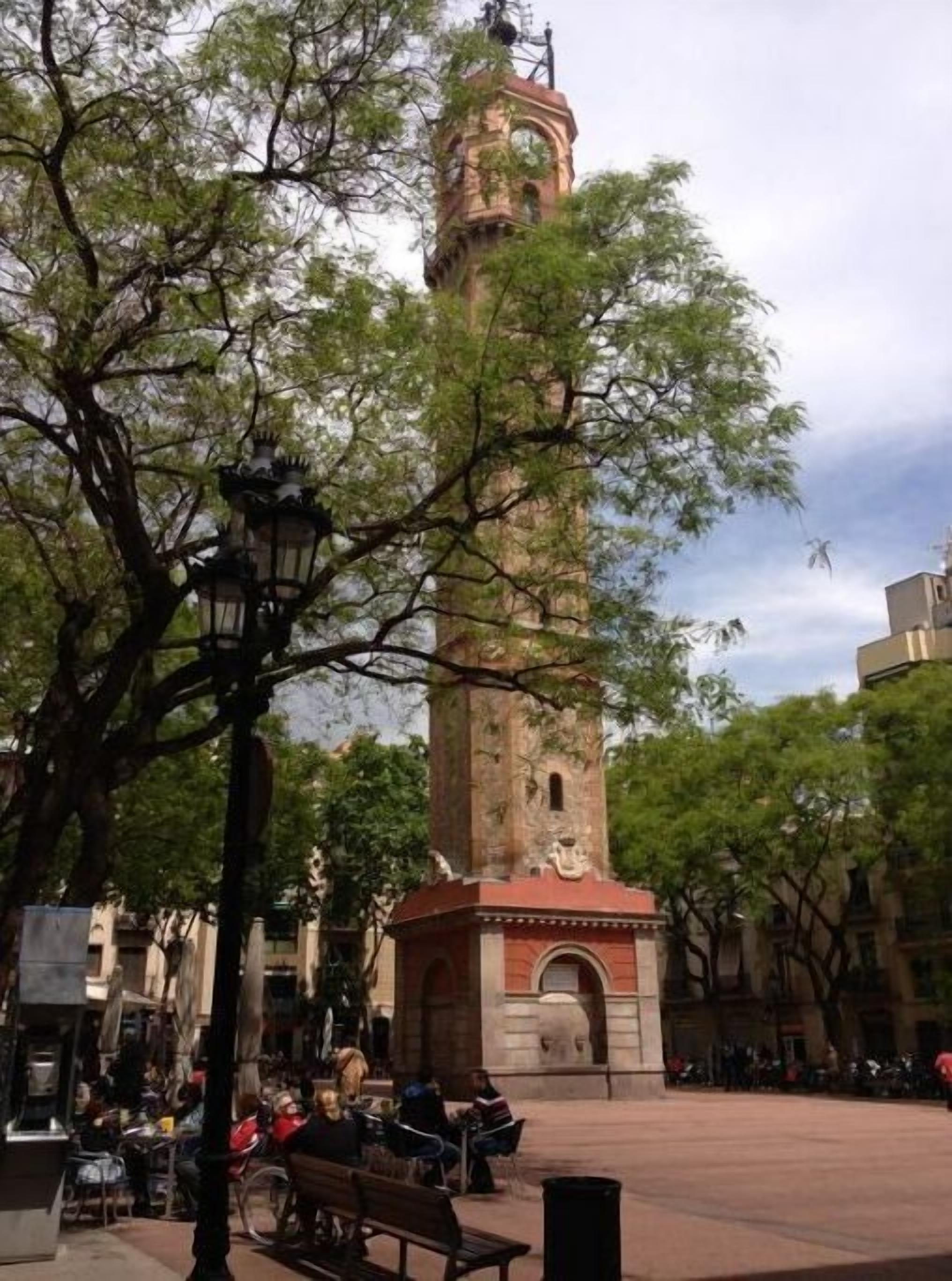 A square with a central tower, benches, and trees.