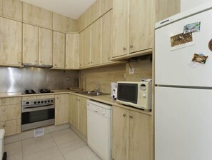 Efficient kitchen with a stainless steel range hood, white dishwasher, and microwave, along with a sink and small window.