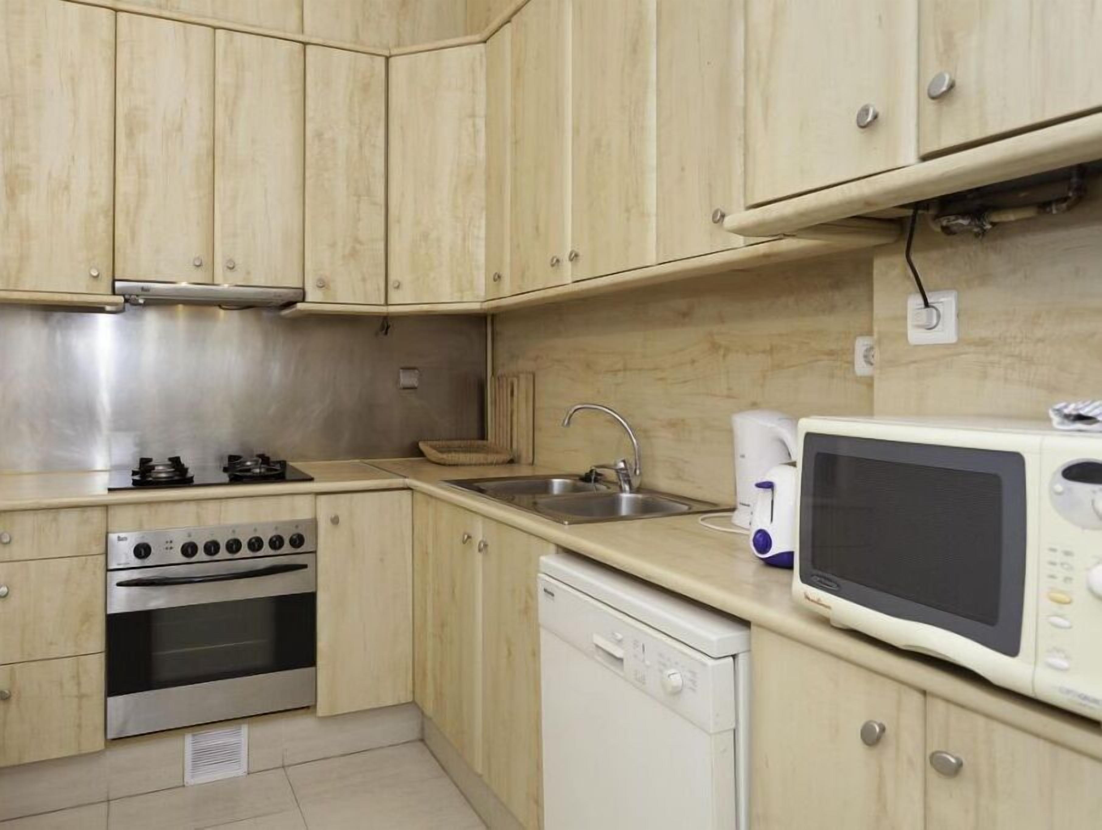 Una cocina compacta con armarios de madera, una estufa de acero inoxidable, un lavamanos, un microondas y un lavavajillas.