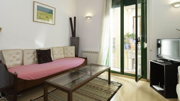 A living room with a sofa, a glass coffee table, a television, and a sliding glass door leading to an outdoor area.