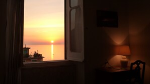 Een kamer met uitzicht op een zonsondergang boven het water, een raam, een lamp en een stoel.