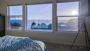 Une chambre à coucher dotée de trois grandes fenêtres donnant sur l’océan et la forêt.