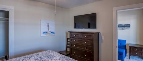 Un dormitorio con una cama, un aparador, un ventilador de techo, un televisor y obras de arte en la pared.
