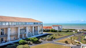 Un edifici de diverses plantes amb un balcó, una zona d'aparcament i vistes al mar.