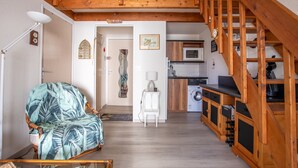 Un saló d'estar acollidor amb una escala de fusta, una cuina amb electrodomèstics moderns i vista a l'exterior.
