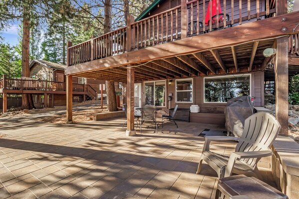 Eine Holzterrasse mit Sitzgelegenheiten im Freien und einem überdachten Bereich, umgeben von Bäumen.