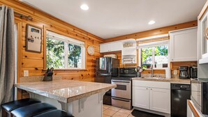 Una cocina moderna con paneles de madera, encimera de granito, electrodomésticos de acero inoxidable y un taburete de bar.
