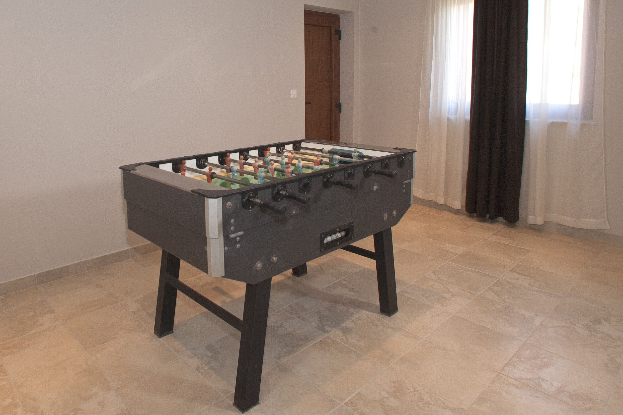 A foosball table in a room with tiled flooring and a door in the background.